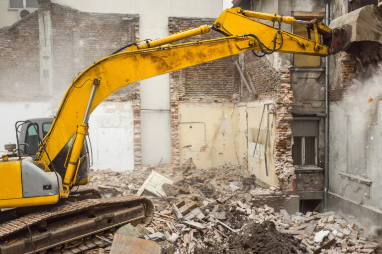 Escavadeira hidráulica amarela realizando demolição mecânica de edifício com entulho no chão